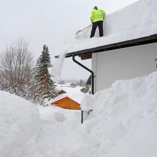A man shovels dangerously heavy snow from a house roof