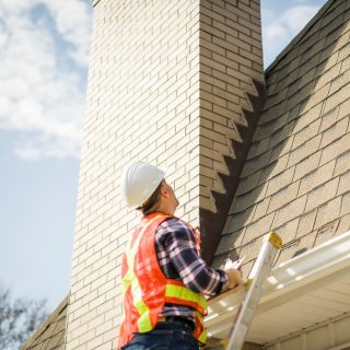 A man with hard hat standing on steps inspecting house roof