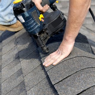 A roofer nails shingles over ridge vent material used on the peak of new residential house construction.